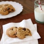 Gluten-free brown butter chocolate chip cookies on a napkin. A glass of milk and a platter of cookies is in the background.