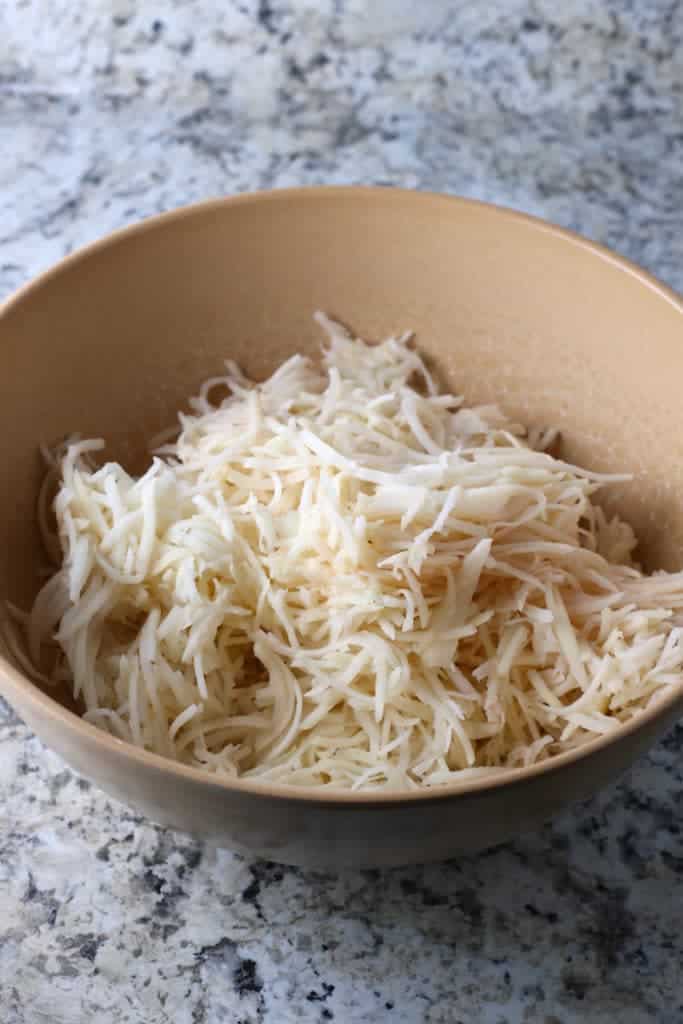 Shredded potatoes and onion in a brown bowl.