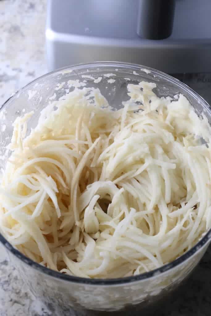 Shredded potatoes in the bowl of a food processor.
