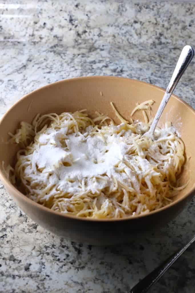 Gluten-Free latkes mixture in a brown bowl with rice flour sprinkled on top.