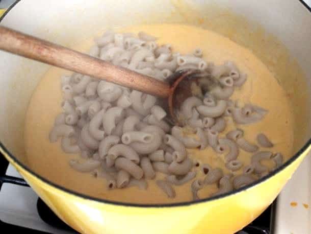 Stirring cooked macaroni into gluten-free cheese sauce.