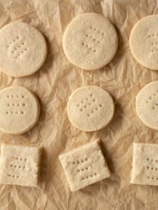 Gluten-free shortbread cookies on a crinkled brown piece of parchment paper. The top two rows are round cookies. The bottom row are square cookies.