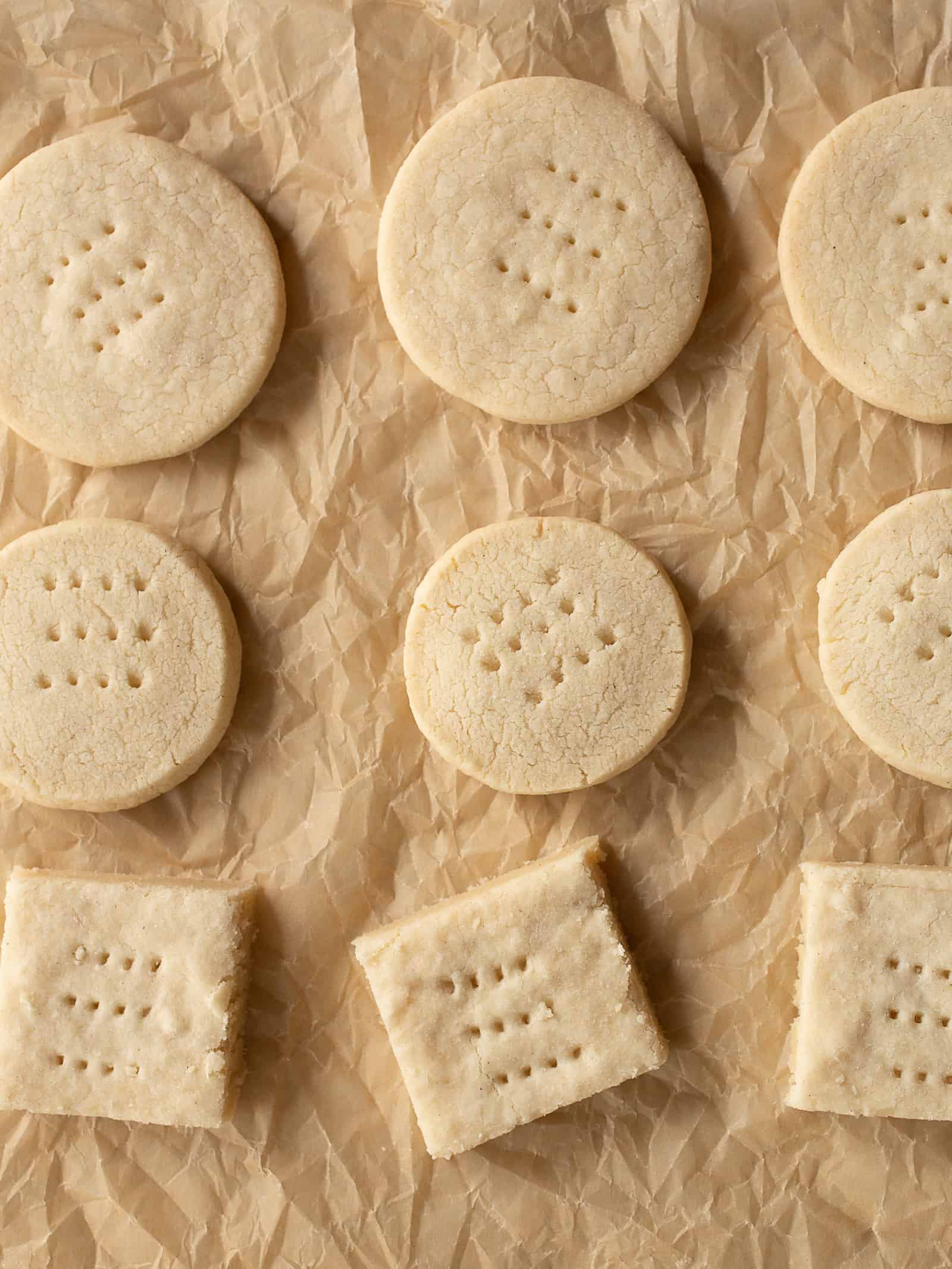 Gluten-free shortbread cookies on a brown, wrinkled piece of parchment paper. Two rows of round cookies and one row of square cookies.