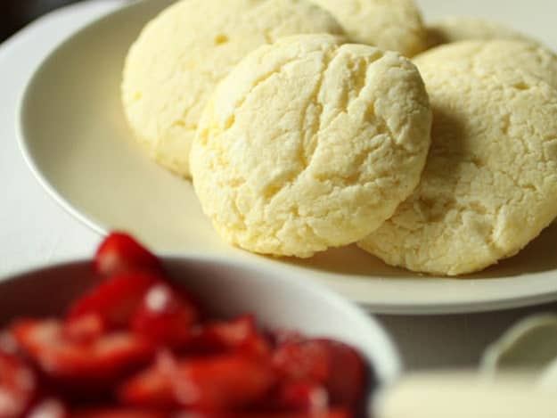 Gluten-Free Strawberry Shortcakes on a plate. A bowl of strawberries sits next to the plate of shortcakes.