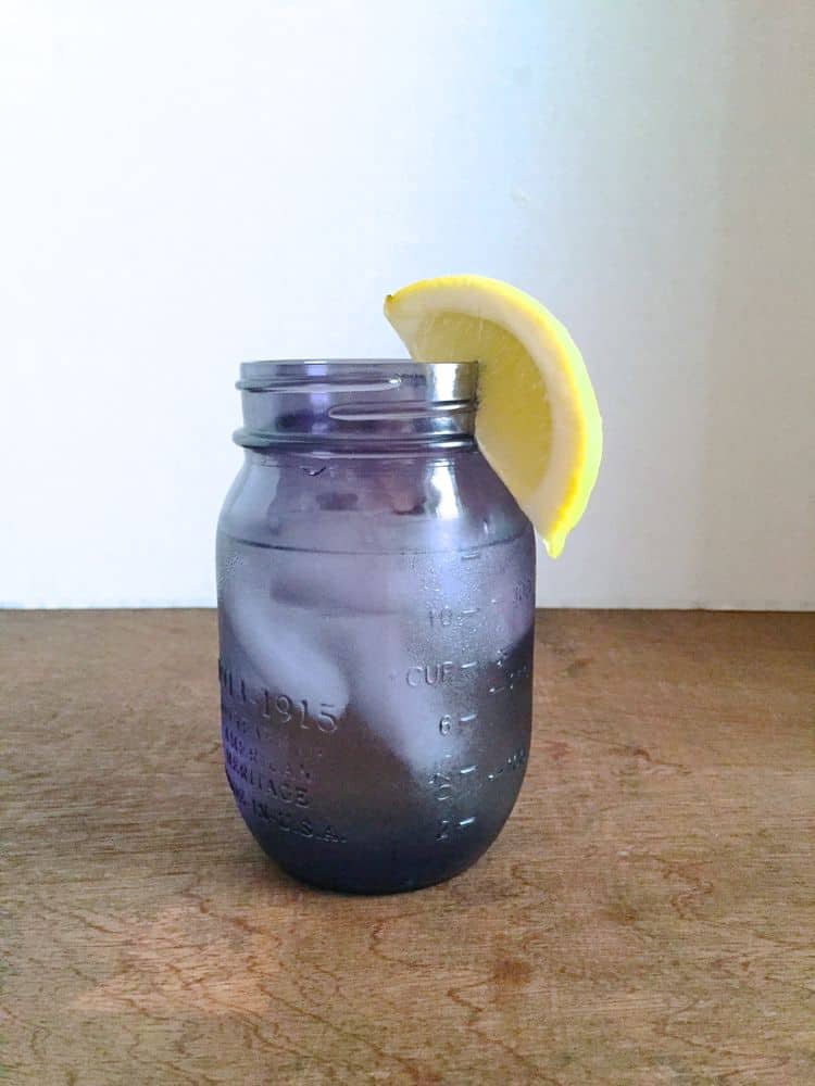 Purple Ball Glass filled with iced water. A lemon wedge is on the side of the glass.