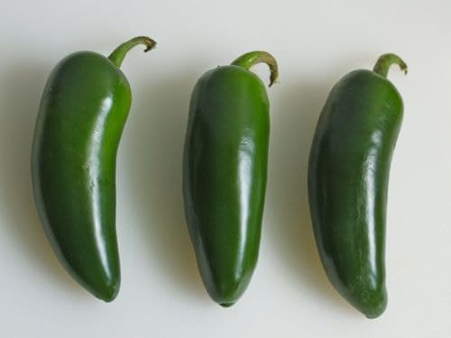 Three jalapeño peppers on a white cutting board.