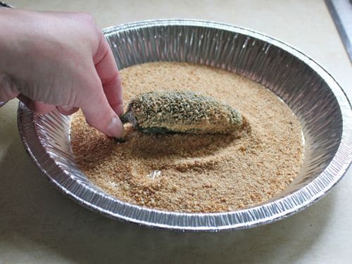 Rolling jalapeño pepper in gluten-free bread crumbs.