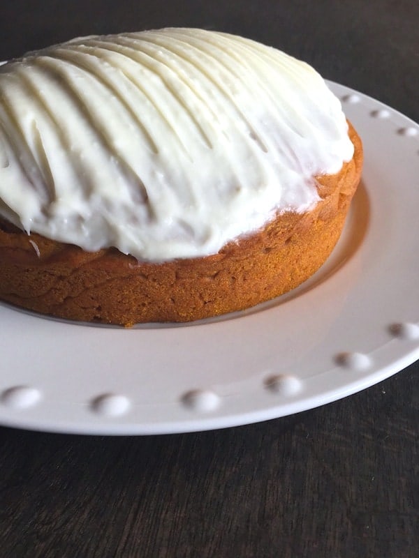 Gluten-free pumpkin cake frosted with cream cheese frosting on white platter.