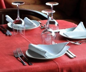 Table set with glasses, flatware, silverware, and red tablecloth.