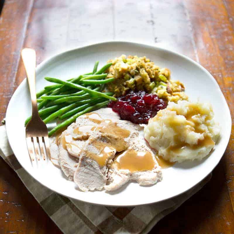 Gluten-free gravy on turkey on a plate of Thanksgiving food.