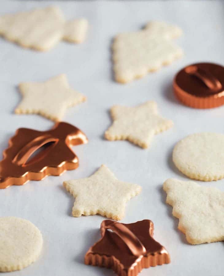 Baked paleo sugar cookies on a pan with three cookie cutters.