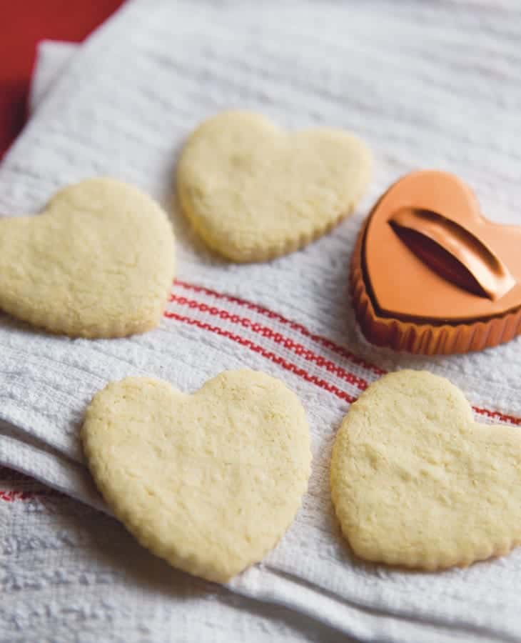 Paleo sugar cookie hearts on white towel with cookie cutter.