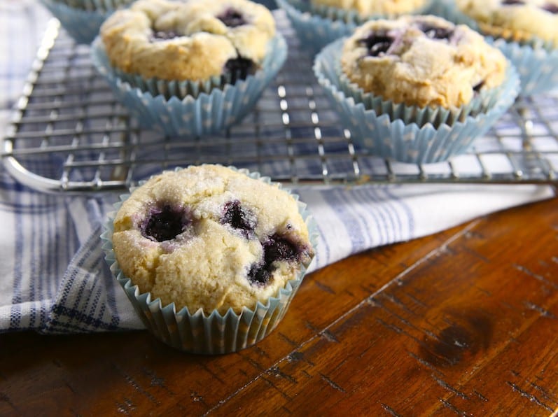 Gluten-free blueberry muffins on a wire rack. One muffin is sitting in front of the rack.