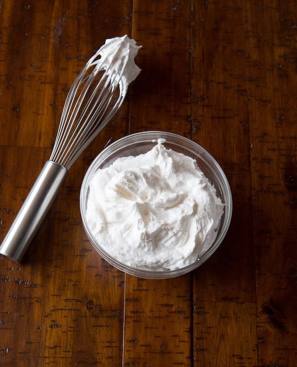 Whipped cream in a glass bowl. A whisk sits next to it.