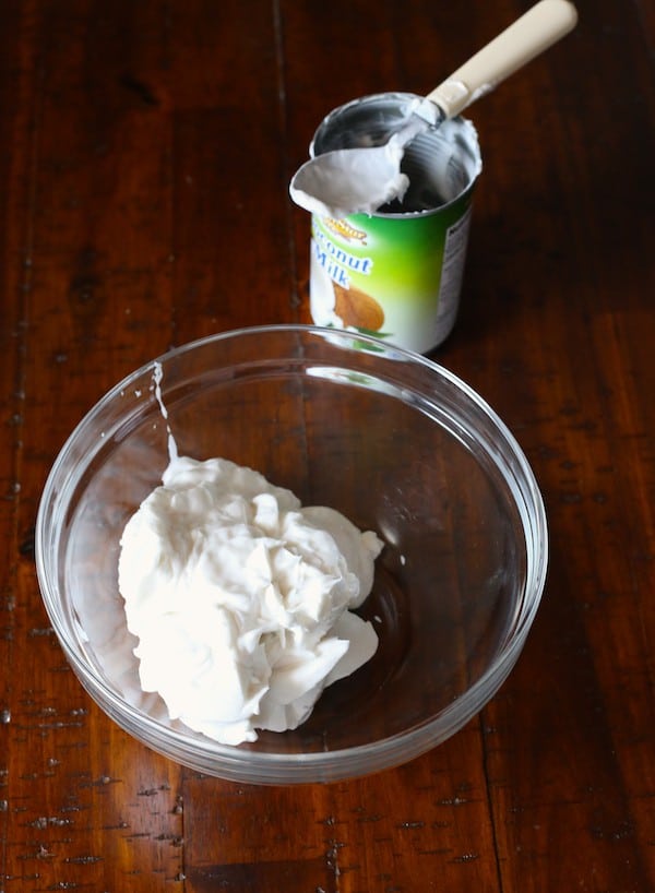Coconut milk in a glass bowl. A can of coconut milk sits behind it.