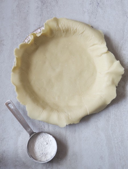 Gluten Free Pie Crust in a pan. Measuring cup of flour sits next to it.