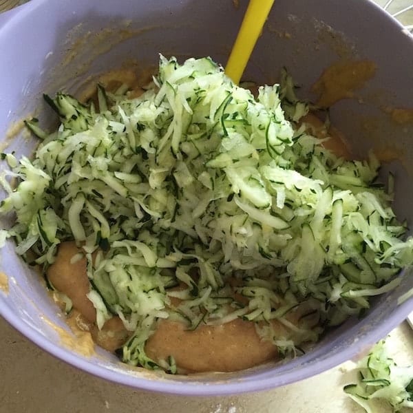 Grated zucchini being added to gluten-free zucchini bread batter.