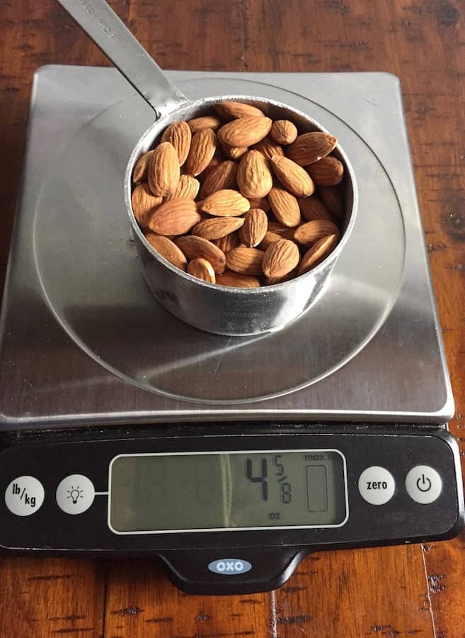 Measuring cup filled with almonds on a digital scale. Display reads 4 5/8 ounces.