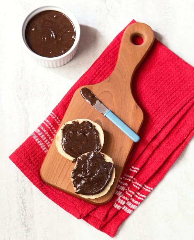 Chocolate almond butter spread on a biscuit. A bowl of chocolate almond butter sits alongside.