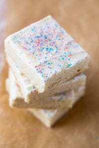 Stack of gluten-free sugar cookie bars. Frosted with vanilla frosting and topped with sprinkles.