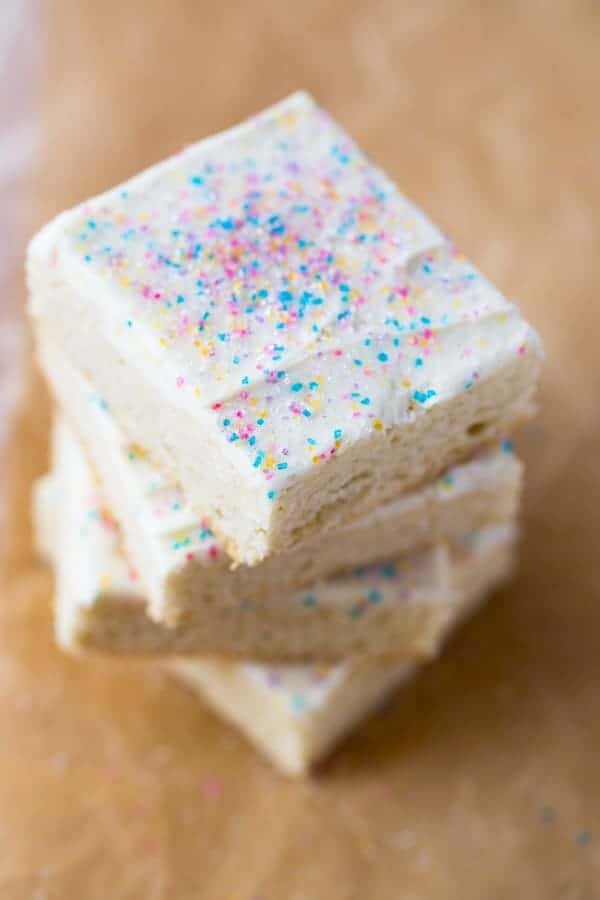 Stack of gluten-free sugar cookie bars. Frosted with vanilla frosting and topped with sprinkles.