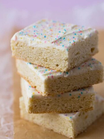 Stack of gluten-free sugar cookie bars. Frosted with vanilla frosting and topped with colored sugar.