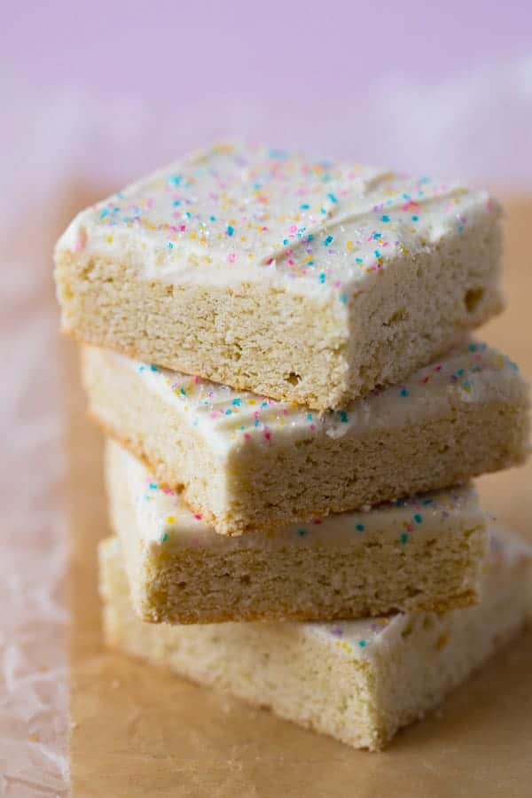 Stack of gluten-free sugar cookie bars. Frosted with vanilla frosting and topped with spinkles.