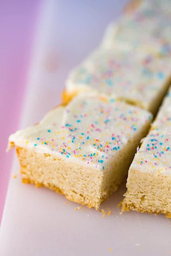 Gluten-free sugar cookie bars on cutting board. Frosted with vanilla frosting and topped with colored sugar.