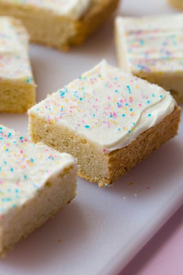 Gluten-free sugar cookie bars on cutting board. Frosted with vanilla frosting and topped with colored sugar.