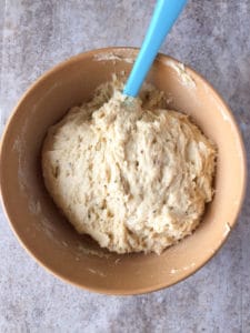 Bowl of gluten-free Italian Easter bread dough in wood bowl with blue spatula.