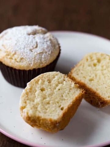 Gluten-free sour cream muffins topped with powdered sugar. One is split to show texture.