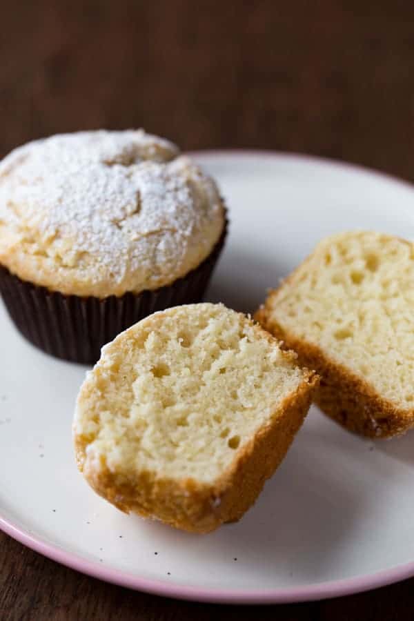 Gluten-free sour cream muffins topped with powdered sugar. One muffin is split to show texture.