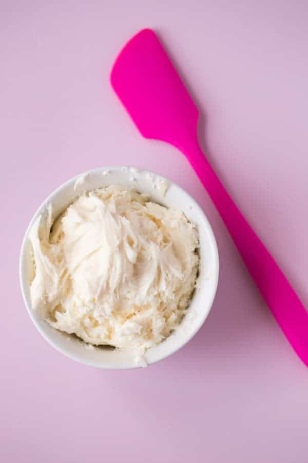 Gluten-Free Vanilla Buttercream Frosting in a white bowl with a pink spatula next to it.
