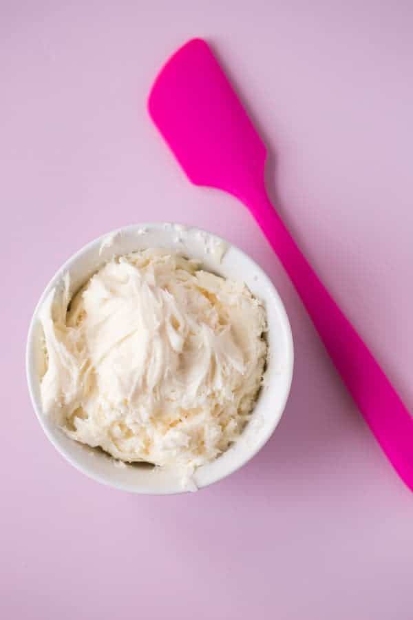 Gluten-Free Vanilla Buttercream Frosting in a bowl with a pink spatula next to it.