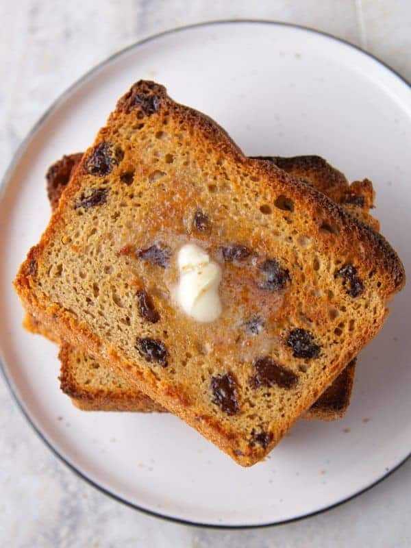 Stack of toasted cinnamon raisin bread slices. Melted butter on top slice. 