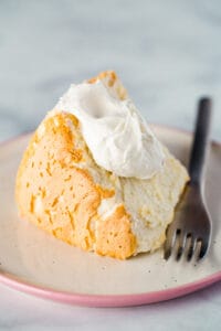 Gluten-free angel food cake with whipped cream on plate.