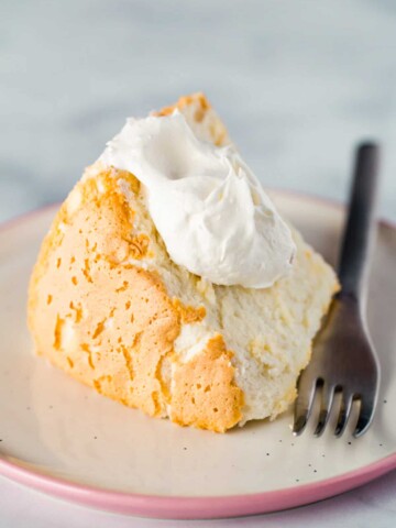 Gluten-free angel food cake with whipped cream on plate.