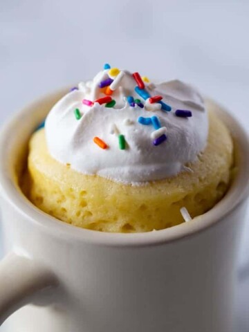 Gluten-Free Mug Cake in White Mug. Topped with Whipped Cream and Sprinkles