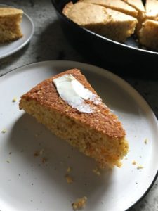 Slice of gluten-free cornbread on plate with butter on top.