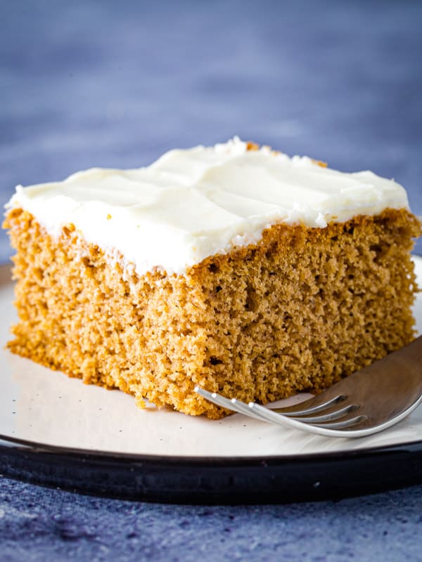Slice of gluten-free spice cake with cream cheese frosting on plate. 