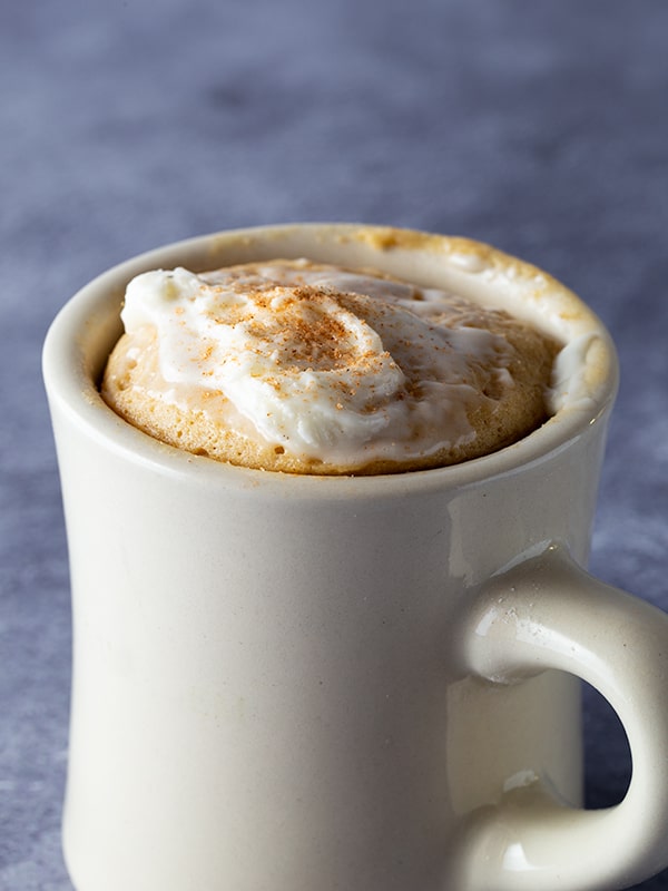 Mug with gluten-free spice mug cake in it. Frosted with cream cheese frosting and sprinkled with ground cinnamon.