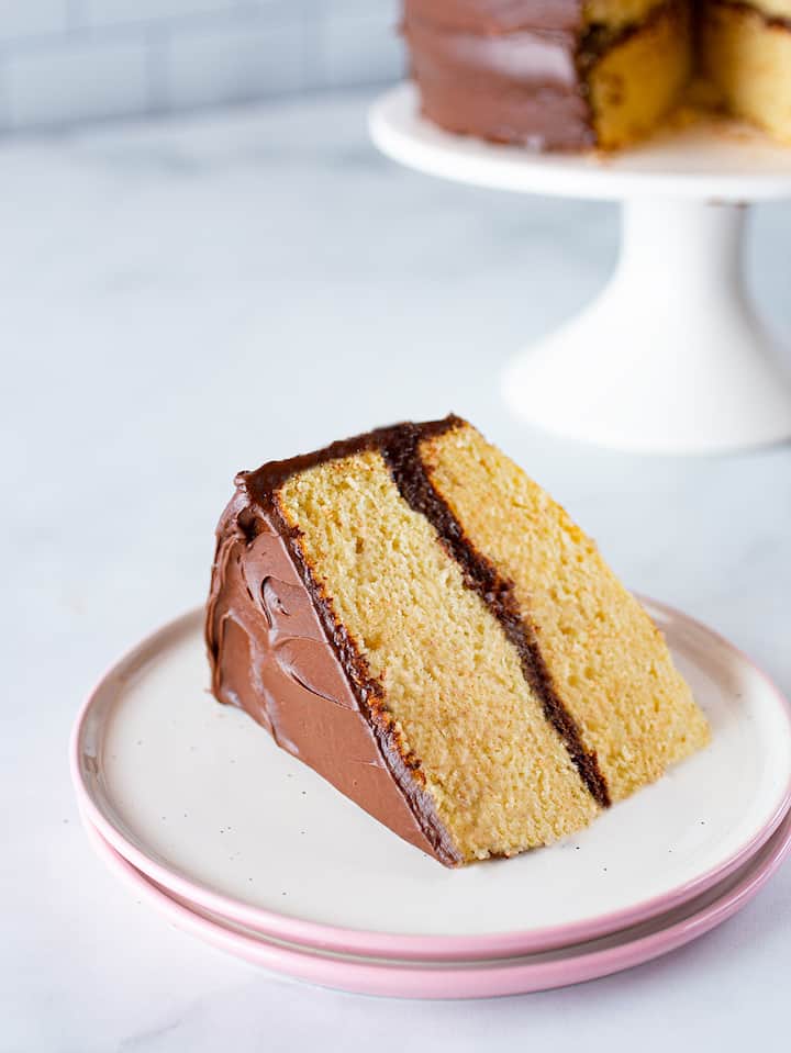 Slice of gluten-free yellow cake on white plate with pink edge. 