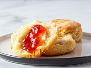 Gluten-free biscuit, split on a plate, topped with jam.