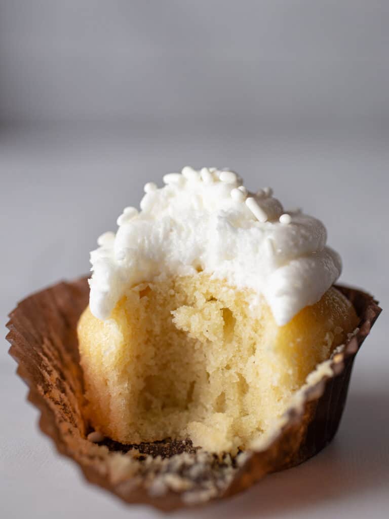 Gluten-free vanilla cupcake. Frosted with vanilla frosting. Bite taken out.
