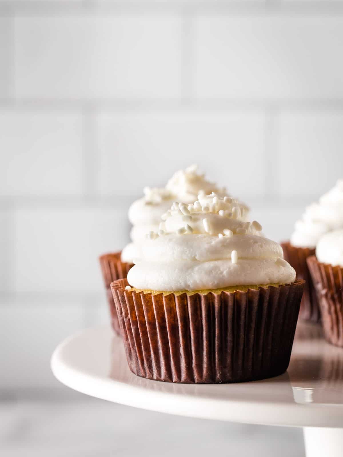 Gluten-free vanilla cupcakes with white frosting on a cake platter.