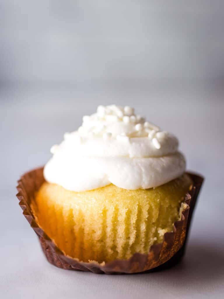 Gluten-Free vanilla cupcake. White frosting. Unwrapped in front.