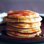 Almond flour pancakes stacked on a plate with maple syrup.