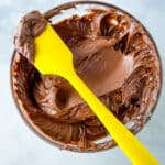 Bowl of gluten-free chocolate frosting with yellow spatula.