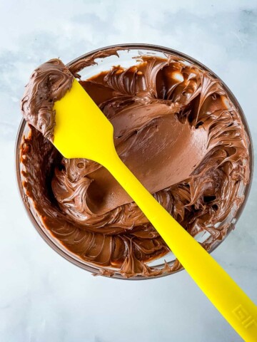 Bowl of gluten-free chocolate frosting with yellow spatula.