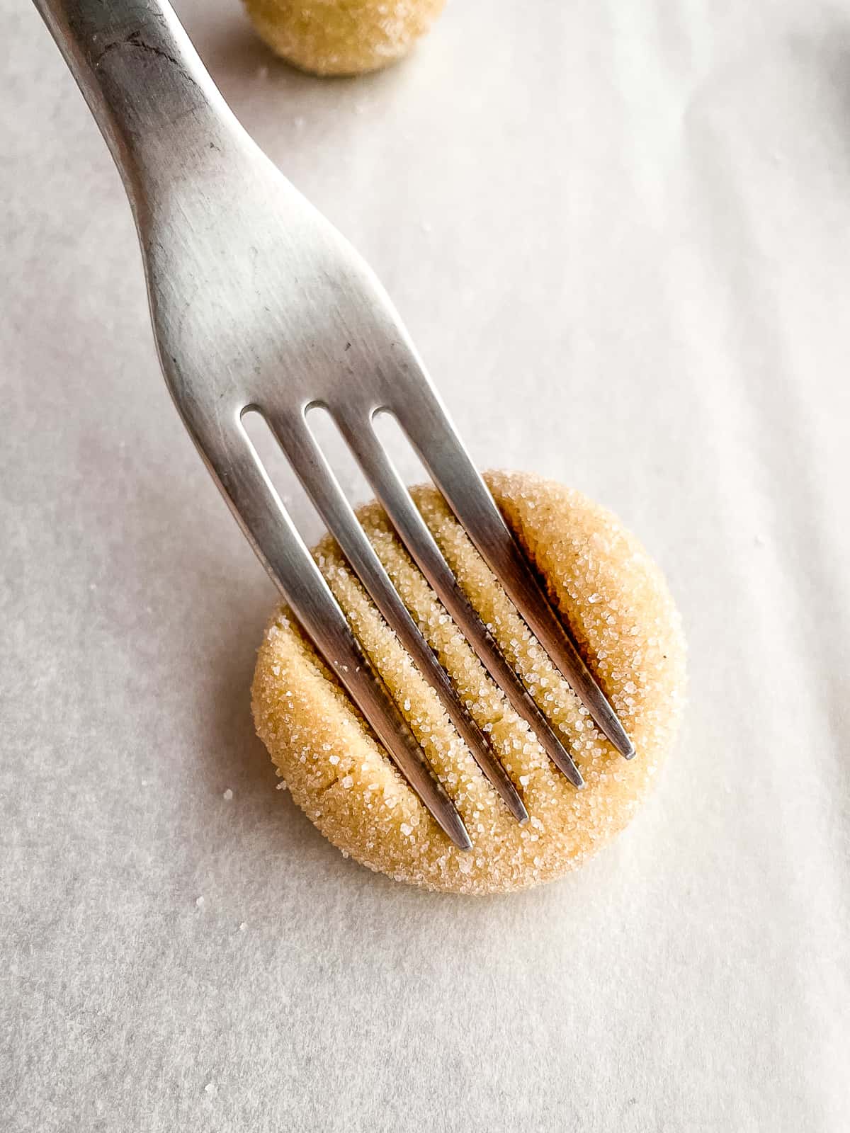 Fork pressing lines into a gluten-free peanut butter cookie.